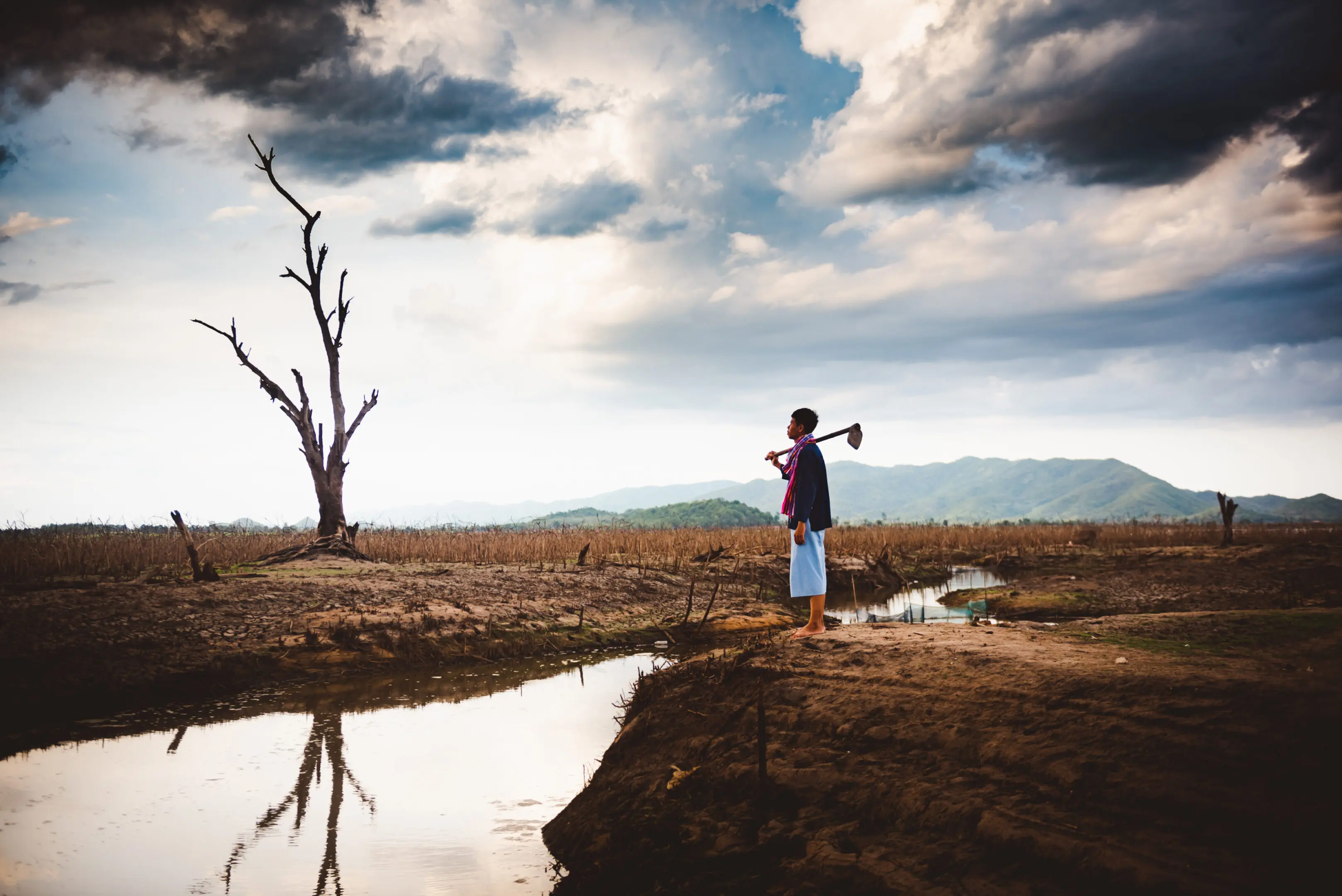 A person playing violin near a reflective water body under a cloudy sky.