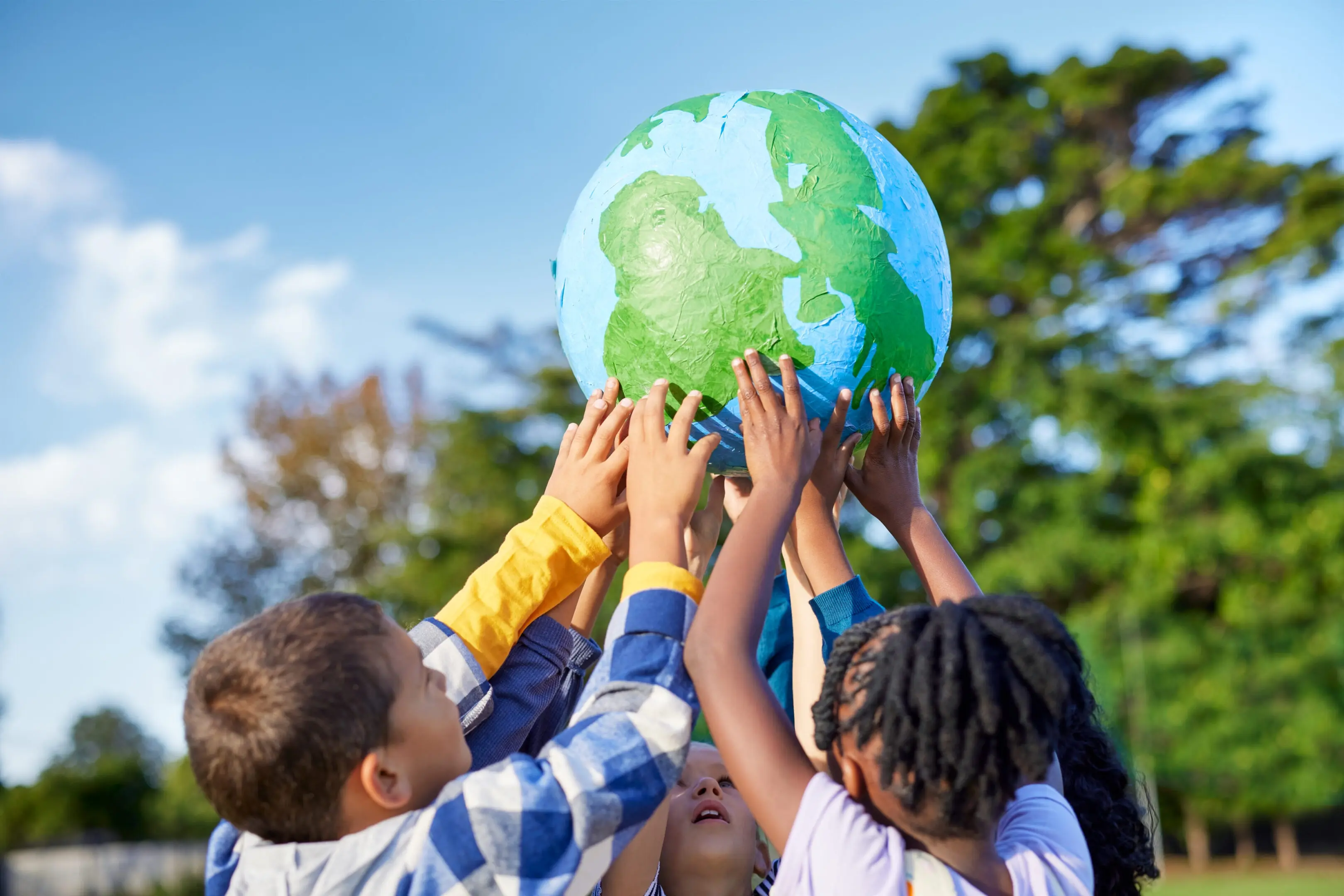 Children holding up a globe together outdoors.