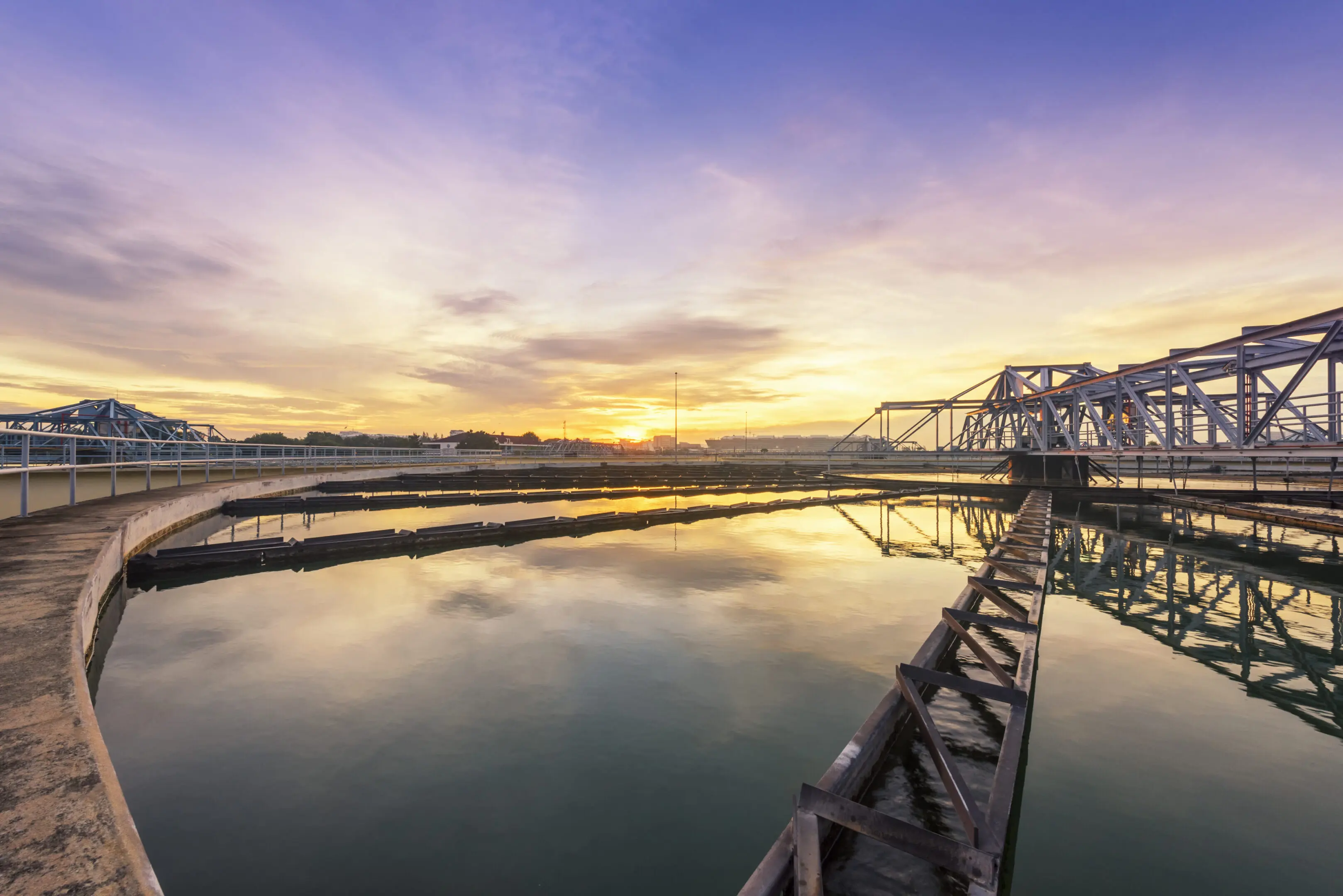 Sunset over a calm river with a bridge and industrial structures.