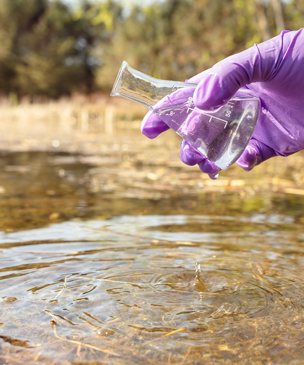 A gloved hand collecting water from a stream.